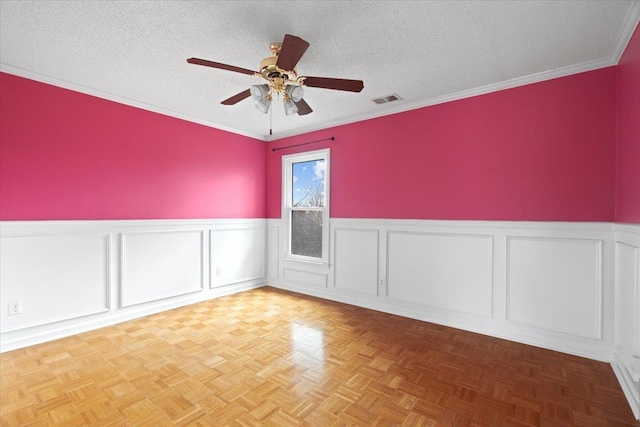 unfurnished room featuring a textured ceiling, wainscoting, visible vents, and a ceiling fan