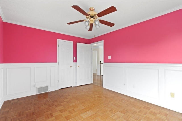 spare room with a ceiling fan, a wainscoted wall, visible vents, and a textured ceiling