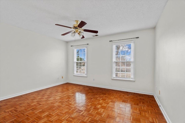 spare room with a textured ceiling, ceiling fan, visible vents, and baseboards