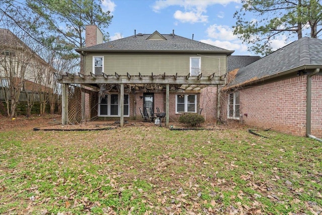 back of property featuring brick siding, a yard, a chimney, and a pergola