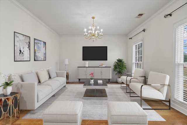 living area featuring ornamental molding, light wood-type flooring, visible vents, and an inviting chandelier