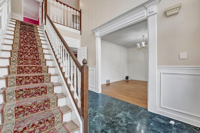 stairs with hardwood / wood-style floors, crown molding, ornate columns, and a chandelier