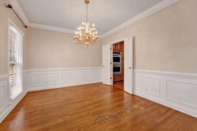 unfurnished room with plenty of natural light, crown molding, an inviting chandelier, and hardwood / wood-style flooring