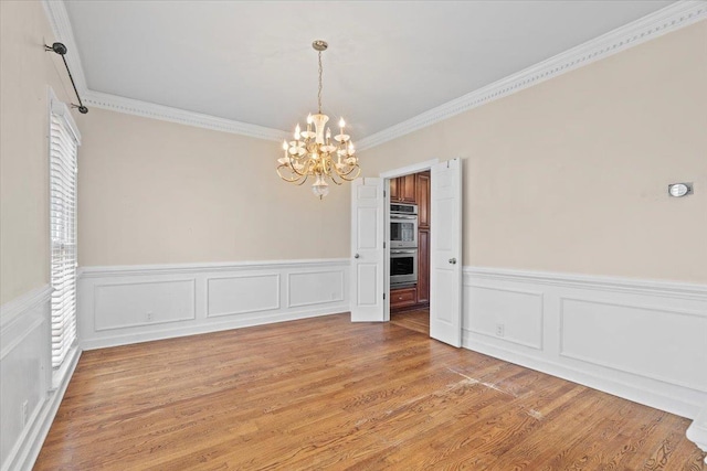 unfurnished room featuring light wood-type flooring, a wainscoted wall, a chandelier, and ornamental molding