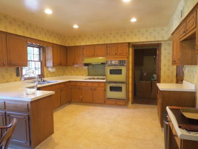 kitchen with double oven, brown cabinets, light countertops, and wallpapered walls