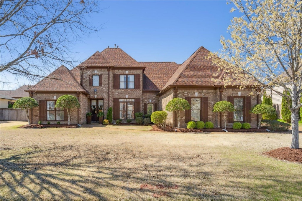 view of front of house with a shingled roof, brick siding, and a front lawn