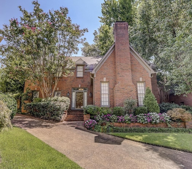 view of front of property featuring brick siding, a chimney, and a front lawn