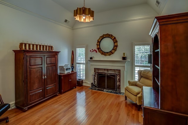 living area with a high end fireplace, visible vents, vaulted ceiling, and light wood-style flooring