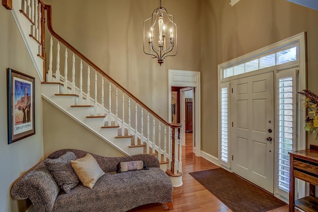 foyer with stairs, wood finished floors, a towering ceiling, and a notable chandelier