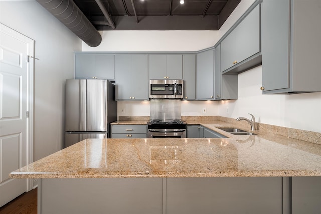 kitchen featuring appliances with stainless steel finishes, a sink, a peninsula, and light stone counters