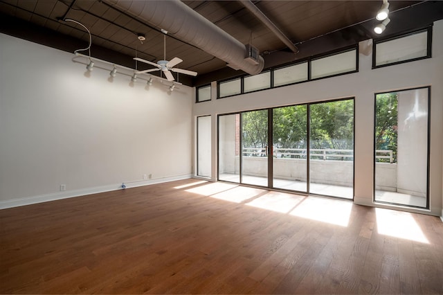 spare room with rail lighting, ceiling fan, baseboards, and wood finished floors