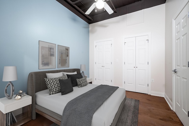 bedroom with a ceiling fan, baseboards, dark wood-style flooring, and multiple closets