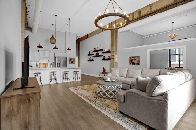 living room featuring high vaulted ceiling, baseboards, light wood-type flooring, beam ceiling, and an inviting chandelier