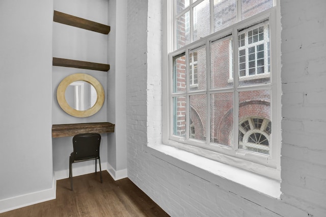 interior space with a wealth of natural light, brick wall, and dark hardwood / wood-style flooring