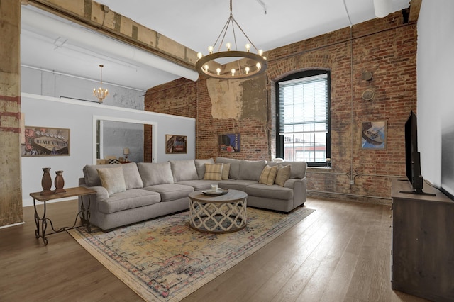 living room with a notable chandelier, beamed ceiling, dark hardwood / wood-style floors, and brick wall