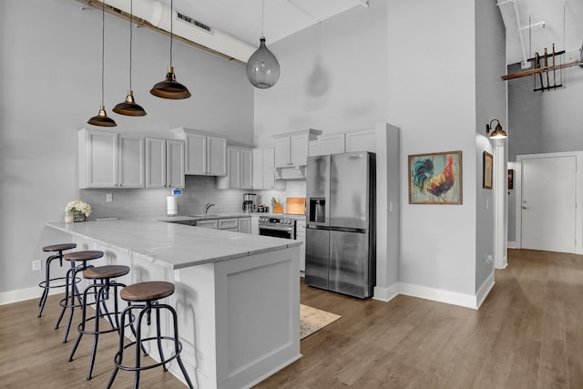 kitchen featuring tasteful backsplash, light wood-type flooring, stainless steel fridge with ice dispenser, kitchen peninsula, and a towering ceiling