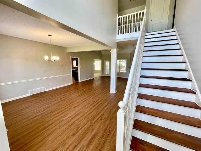 staircase with a towering ceiling, hardwood / wood-style floors, and a chandelier