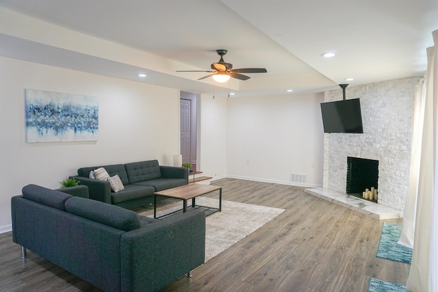 living area with baseboards, dark wood-type flooring, a tray ceiling, a fireplace, and recessed lighting