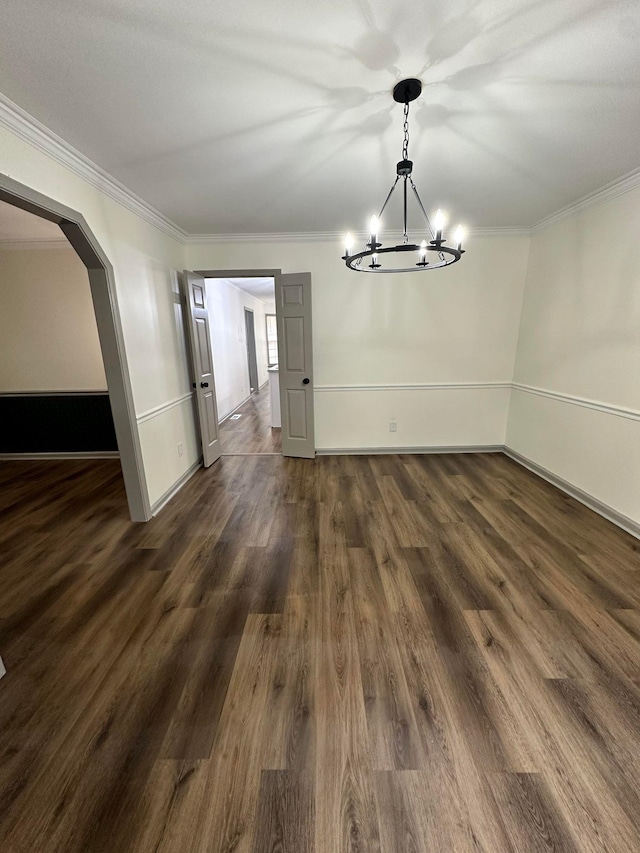 unfurnished dining area with dark wood finished floors, ornamental molding, and an inviting chandelier