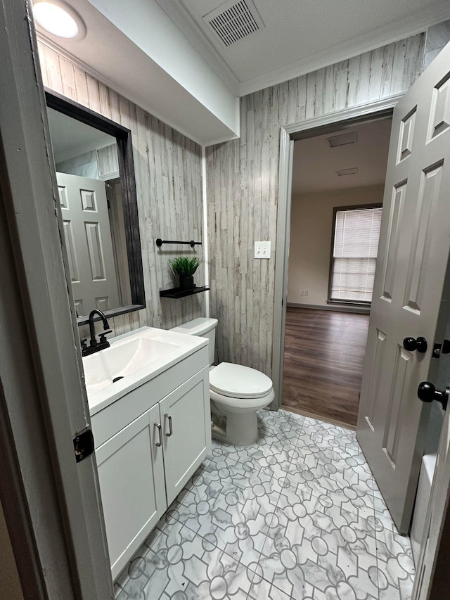 half bath with toilet, visible vents, wooden walls, vanity, and ornamental molding
