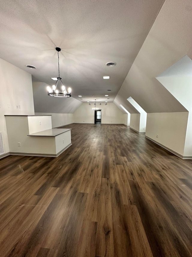 bonus room with a chandelier, lofted ceiling, visible vents, and dark wood-style flooring