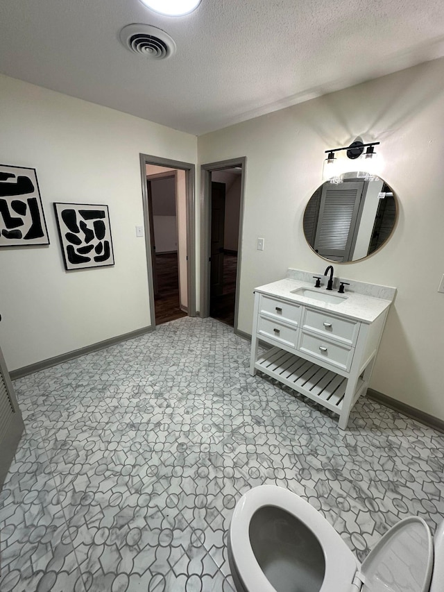 bathroom featuring a textured ceiling, baseboards, visible vents, and vanity