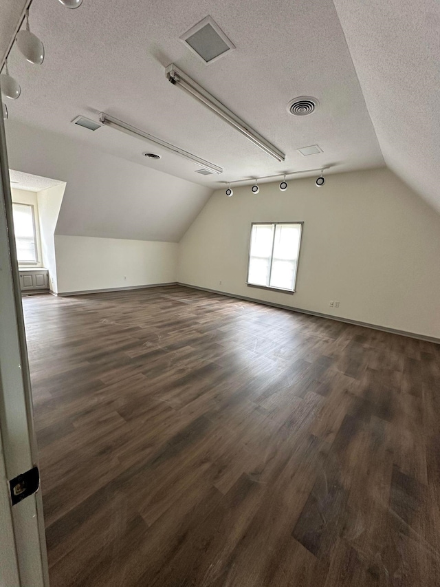 bonus room with dark wood-style floors, vaulted ceiling, visible vents, baseboards, and a textured ceiling