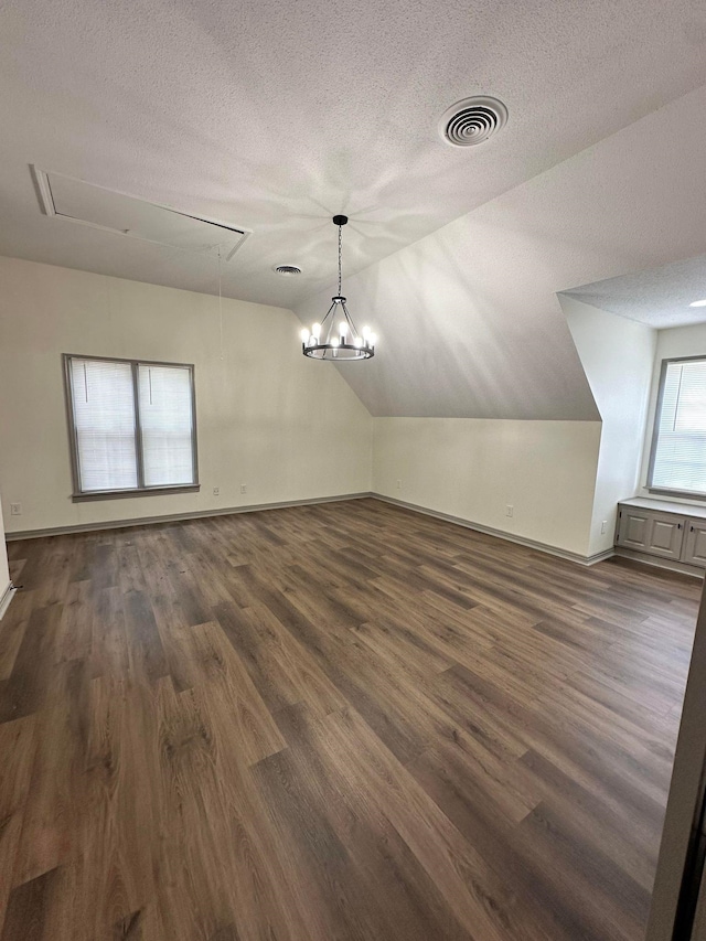 unfurnished dining area featuring a textured ceiling, attic access, dark wood finished floors, lofted ceiling, and visible vents
