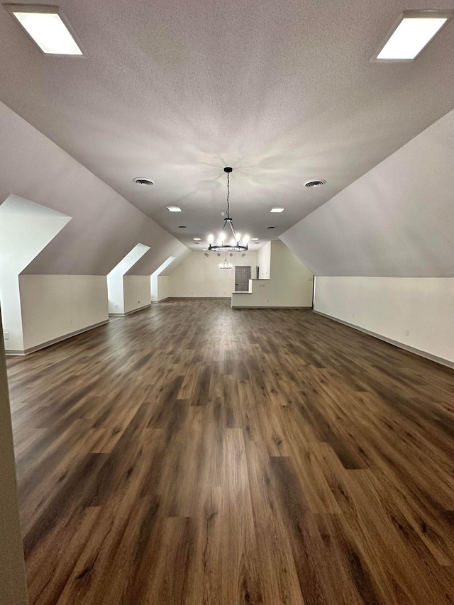 bonus room featuring dark wood-style floors, vaulted ceiling, visible vents, a textured ceiling, and a notable chandelier