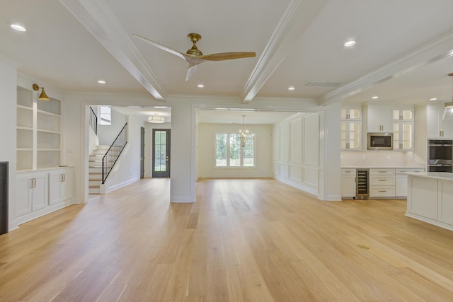 unfurnished living room featuring ceiling fan with notable chandelier, wine cooler, light hardwood / wood-style flooring, ornamental molding, and beam ceiling