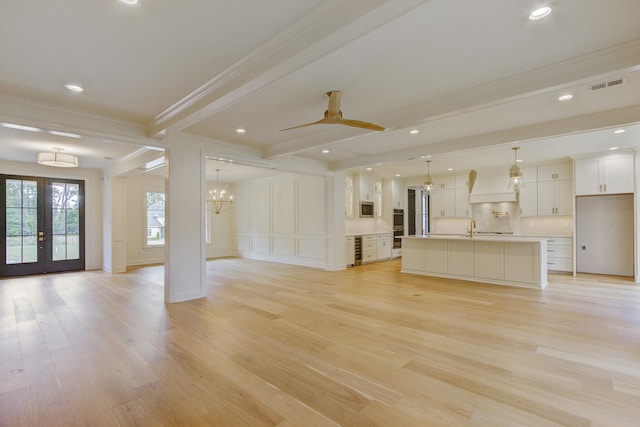 unfurnished living room with french doors, ceiling fan with notable chandelier, light wood-type flooring, ornamental molding, and beam ceiling