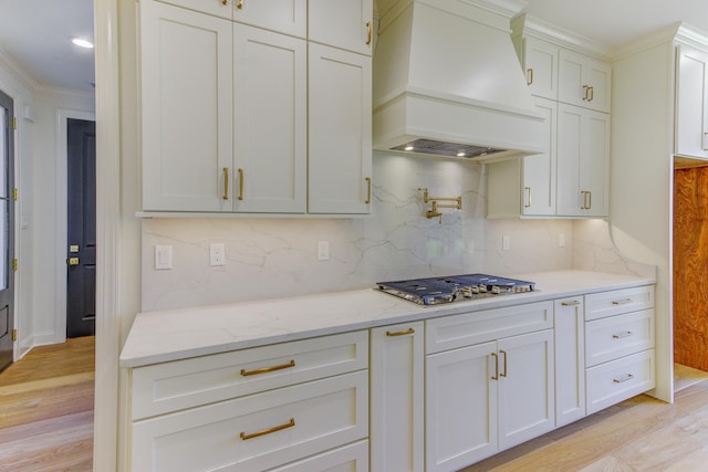 kitchen with stainless steel gas cooktop, tasteful backsplash, light stone counters, light hardwood / wood-style floors, and custom range hood