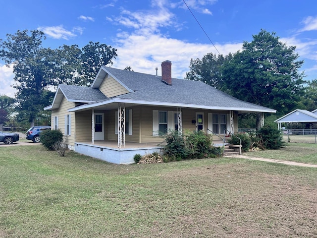 view of front of house featuring a chimney, roof with shingles, covered porch, fence, and a front lawn