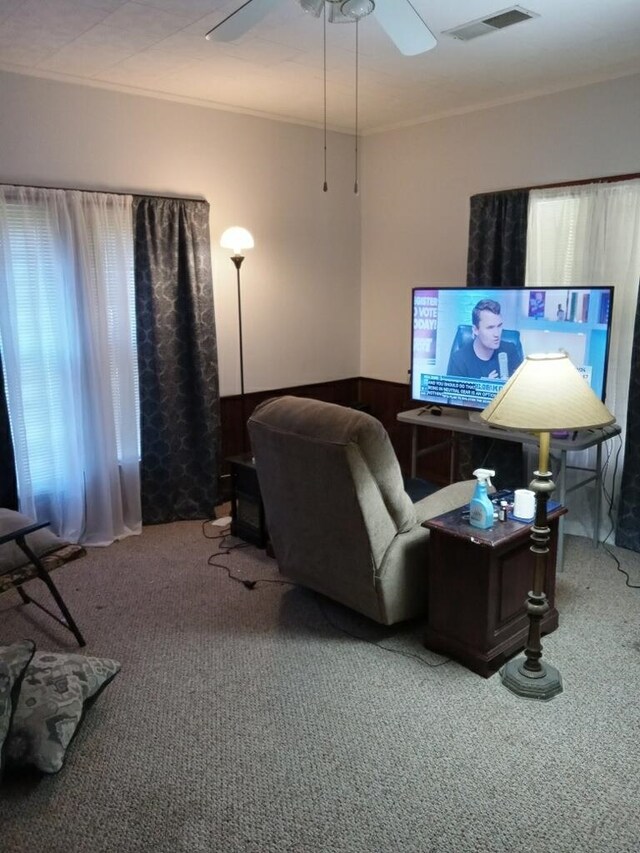 carpeted living room featuring ornamental molding, visible vents, and ceiling fan