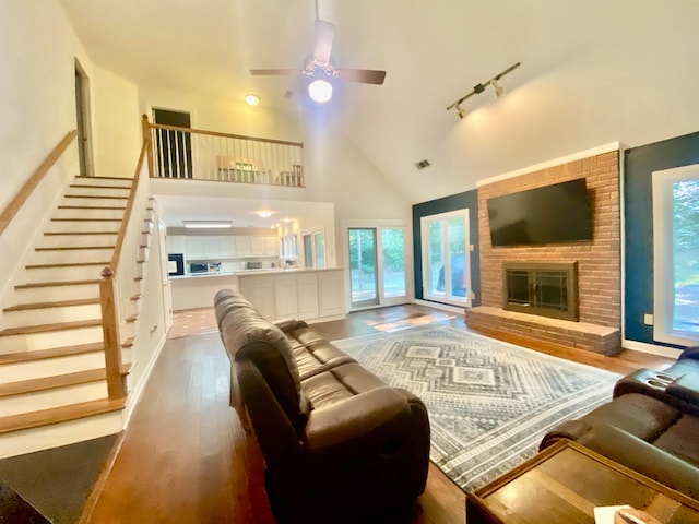 living room with high vaulted ceiling, ceiling fan, wood-type flooring, and a brick fireplace