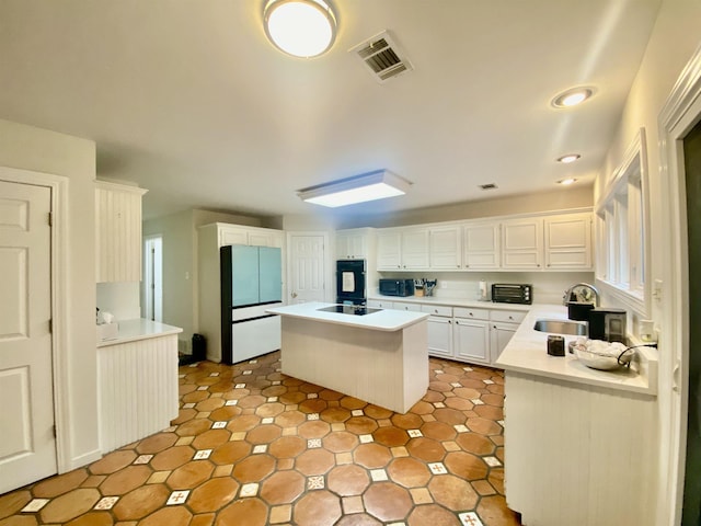 kitchen featuring freestanding refrigerator, a kitchen island, white cabinets, visible vents, and a sink