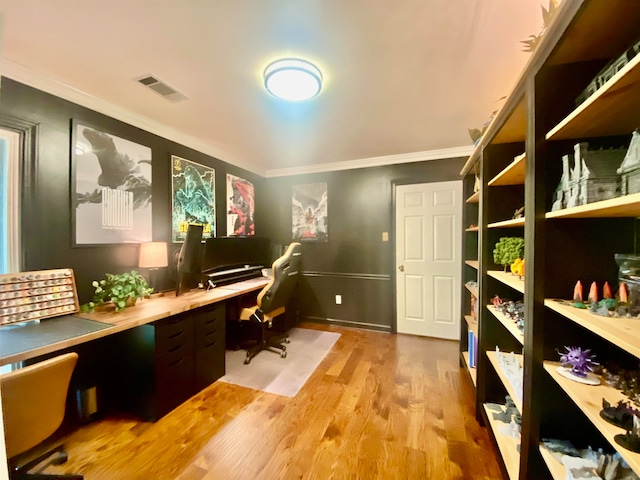 home office featuring light wood-type flooring, ornamental molding, and built in desk