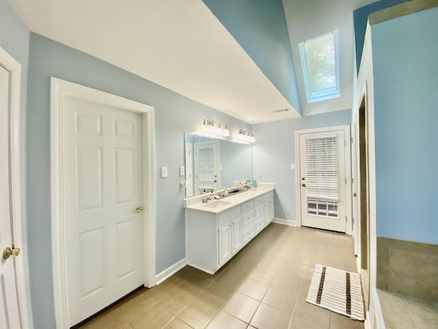bathroom with a skylight, double vanity, baseboards, and tile patterned floors
