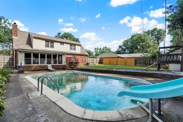 view of swimming pool with a water slide, a sunroom, a lawn, and a patio area