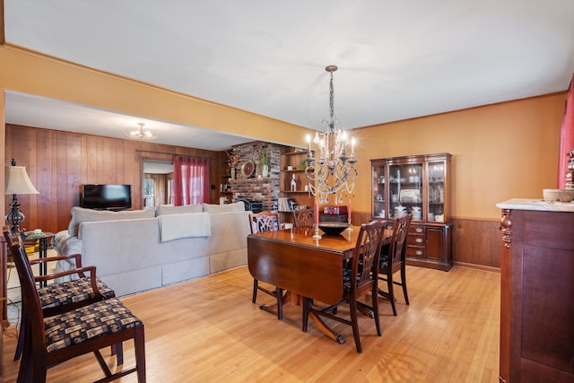 dining space featuring light wood-type flooring, wood walls, a fireplace, and a chandelier