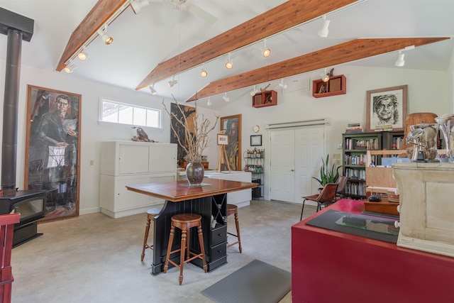 dining area with track lighting, finished concrete floors, lofted ceiling with beams, a wood stove, and a ceiling fan