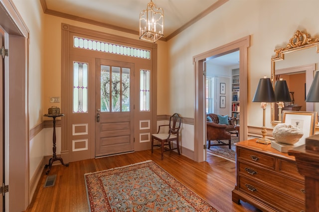 foyer entrance with wood finished floors, a notable chandelier, and ornamental molding