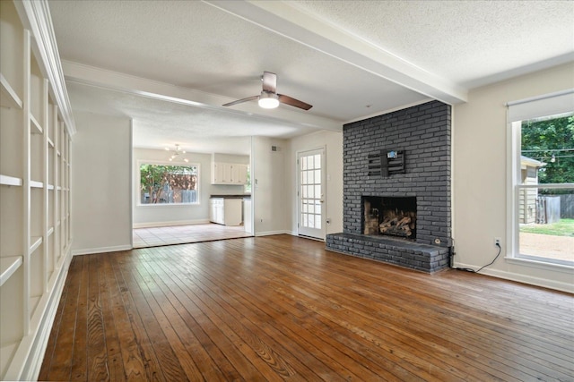 unfurnished living room with a textured ceiling, beamed ceiling, wood-type flooring, a brick fireplace, and ceiling fan