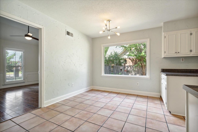 unfurnished dining area with ceiling fan with notable chandelier, light wood-type flooring, and a textured ceiling