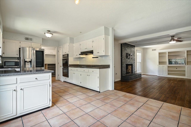 kitchen with light hardwood / wood-style flooring, a brick fireplace, appliances with stainless steel finishes, white cabinetry, and ceiling fan