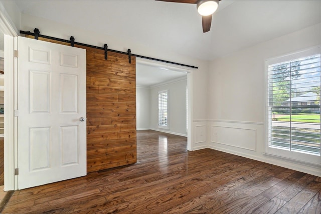 spare room featuring a wealth of natural light, a barn door, ceiling fan, and dark hardwood / wood-style floors