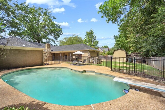 view of pool with a diving board, a shed, and a patio