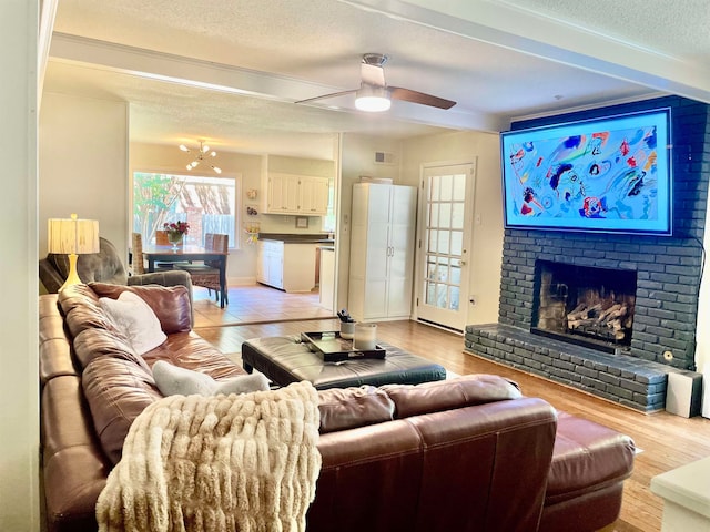 living room with a textured ceiling, light hardwood / wood-style floors, a brick fireplace, plenty of natural light, and ceiling fan