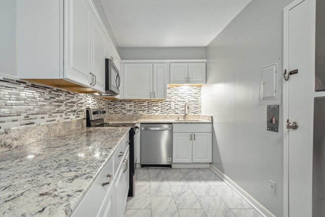 kitchen with light stone countertops, electric panel, stainless steel appliances, white cabinetry, and decorative backsplash