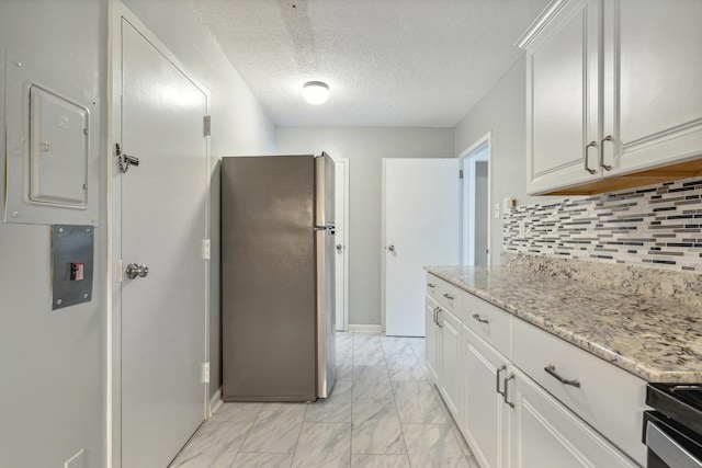 kitchen with a textured ceiling, stainless steel fridge, backsplash, and white cabinetry